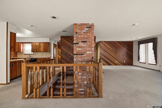 stairway with a textured ceiling, carpet floors, a healthy amount of sunlight, and wood walls