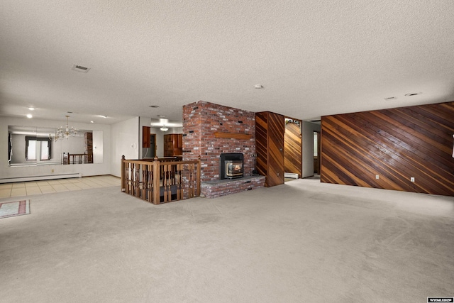 unfurnished living room featuring a textured ceiling, light carpet, wooden walls, a notable chandelier, and a baseboard heating unit