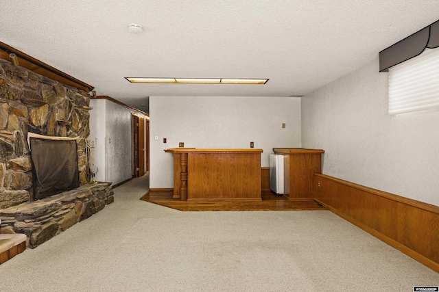 interior space featuring a stone fireplace, wooden walls, light carpet, and a textured ceiling