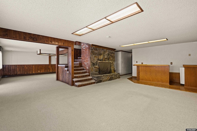 unfurnished living room with a stone fireplace, a textured ceiling, and wood walls