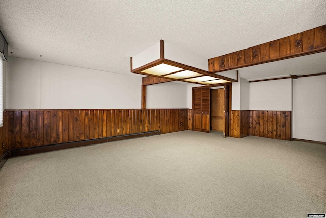 spare room with light carpet, wooden walls, a textured ceiling, and baseboard heating