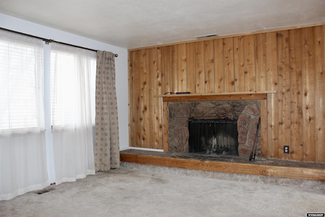 unfurnished living room featuring carpet, a stone fireplace, and wooden walls