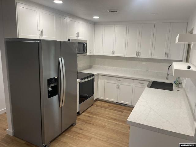 kitchen with light stone countertops, light wood-type flooring, stainless steel appliances, sink, and white cabinets