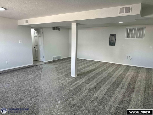 basement featuring dark carpet, a textured ceiling, and electric panel