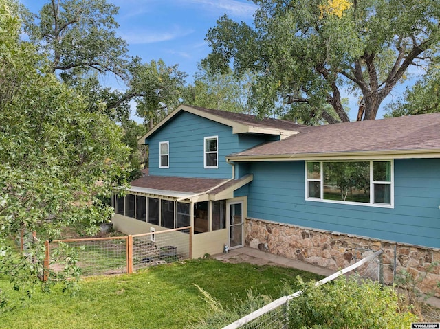 view of front of house featuring a shingled roof, a sunroom, stone siding, fence, and a front lawn