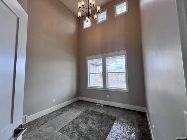 carpeted spare room with a healthy amount of sunlight, a high ceiling, and an inviting chandelier