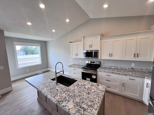 kitchen with a center island with sink, sink, vaulted ceiling, white cabinetry, and stainless steel appliances