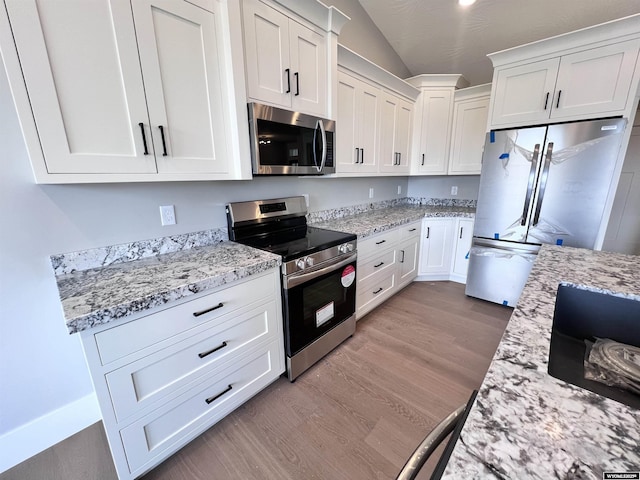 kitchen featuring light stone counters, stainless steel appliances, white cabinets, light hardwood / wood-style floors, and lofted ceiling