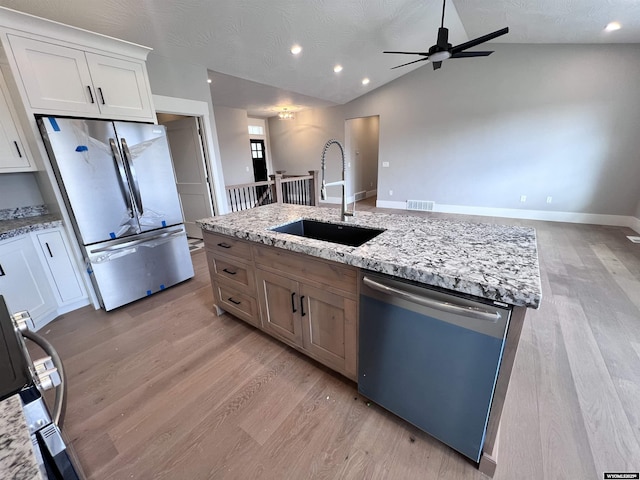 kitchen with appliances with stainless steel finishes, light stone counters, sink, white cabinets, and lofted ceiling