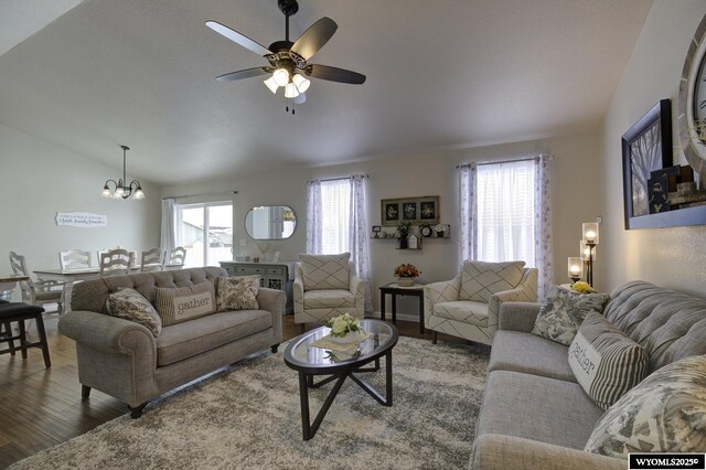 living room with a wealth of natural light, ceiling fan with notable chandelier, dark wood-type flooring, and lofted ceiling