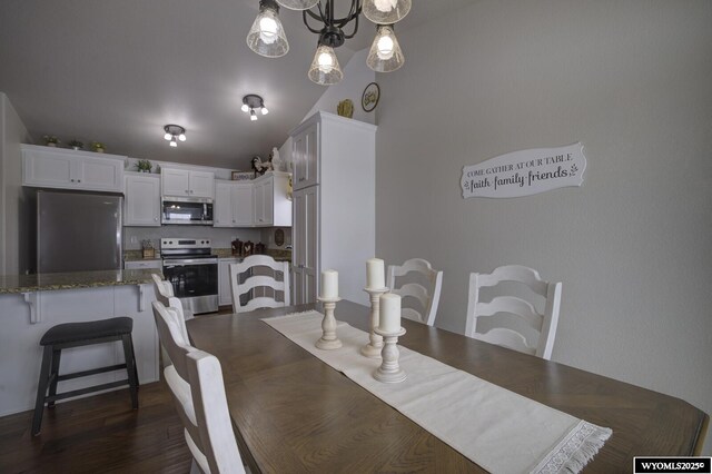 dining space with vaulted ceiling, dark hardwood / wood-style floors, and an inviting chandelier