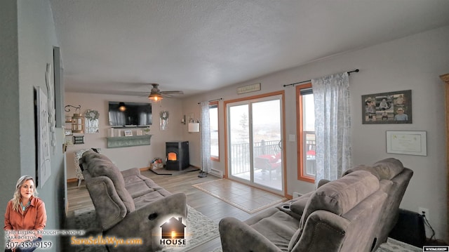 living room featuring ceiling fan, light wood-type flooring, a wood stove, and a textured ceiling