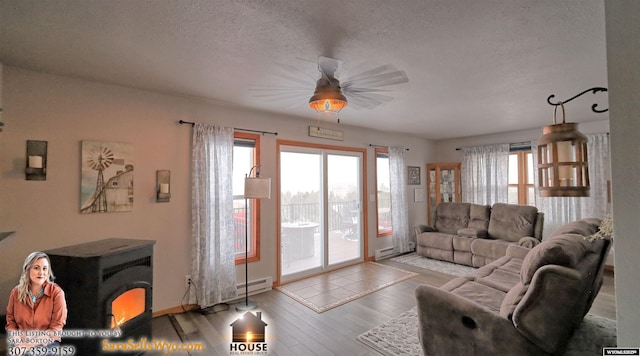 living room featuring a wood stove, ceiling fan, a baseboard radiator, light hardwood / wood-style floors, and a textured ceiling