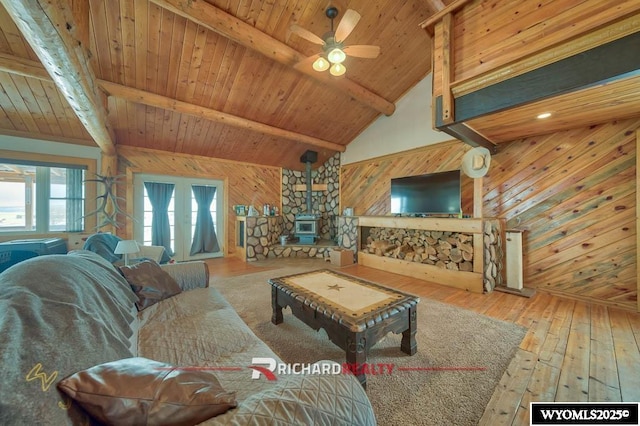 living room with beamed ceiling, a wood stove, wooden walls, and wood ceiling