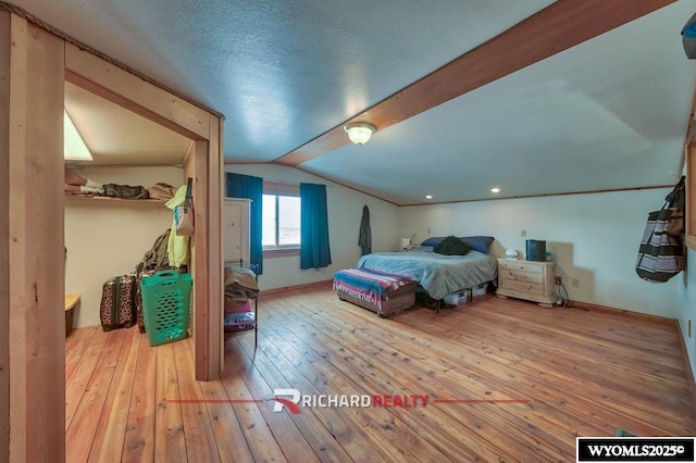 bedroom with a textured ceiling, hardwood / wood-style flooring, and vaulted ceiling