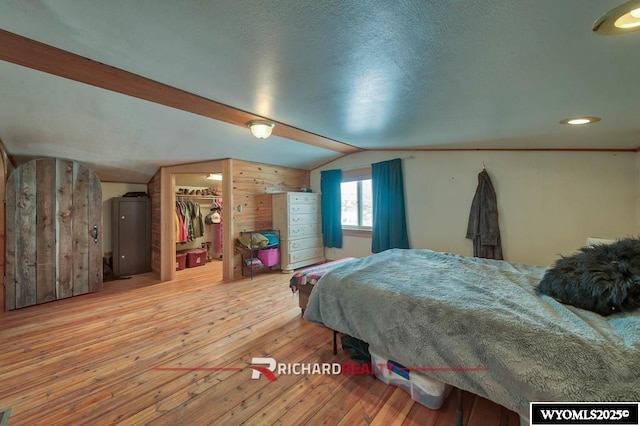 bedroom featuring a walk in closet, hardwood / wood-style floors, a closet, lofted ceiling, and wood walls