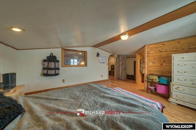 bedroom featuring lofted ceiling, wooden walls, and light hardwood / wood-style flooring