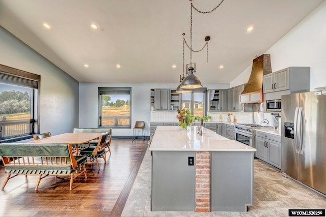 kitchen featuring gray cabinetry, tasteful backsplash, premium range hood, an island with sink, and appliances with stainless steel finishes