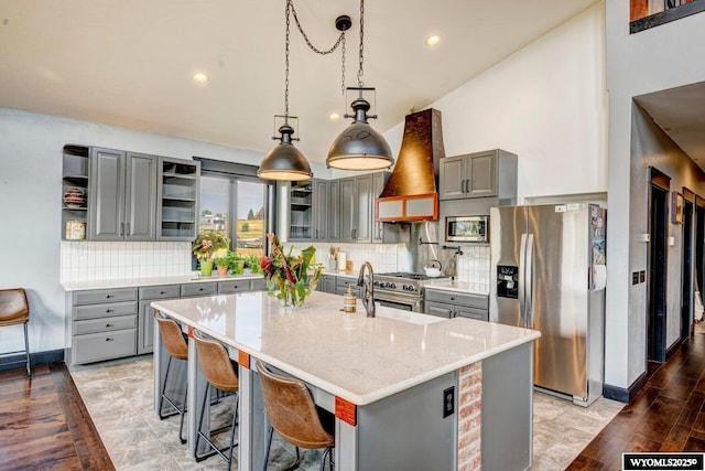 kitchen with gray cabinetry, custom range hood, decorative light fixtures, and appliances with stainless steel finishes