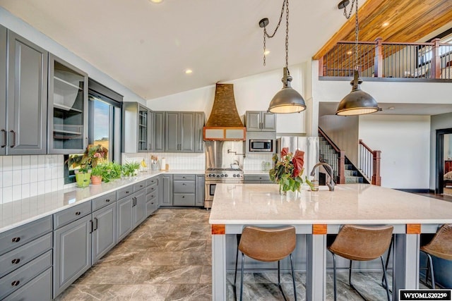 kitchen featuring gray cabinetry, decorative backsplash, premium range hood, and appliances with stainless steel finishes