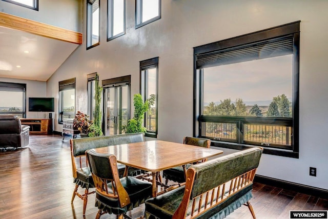 dining space featuring beam ceiling, dark hardwood / wood-style floors, and a high ceiling