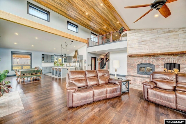 living room featuring ceiling fan, wood-type flooring, high vaulted ceiling, and a brick fireplace