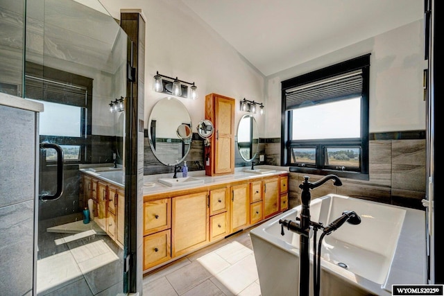 bathroom with tile patterned floors, vaulted ceiling, a bathtub, vanity, and tile walls