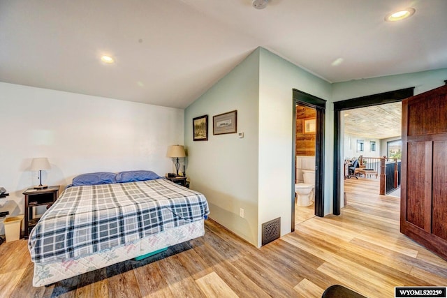 bedroom featuring light hardwood / wood-style floors, lofted ceiling, and connected bathroom