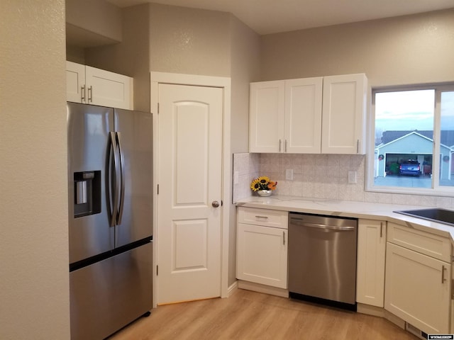 kitchen featuring white cabinetry, sink, stainless steel appliances, light hardwood / wood-style flooring, and backsplash