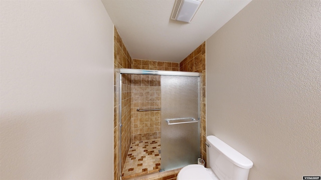 bathroom featuring a shower with shower door and toilet