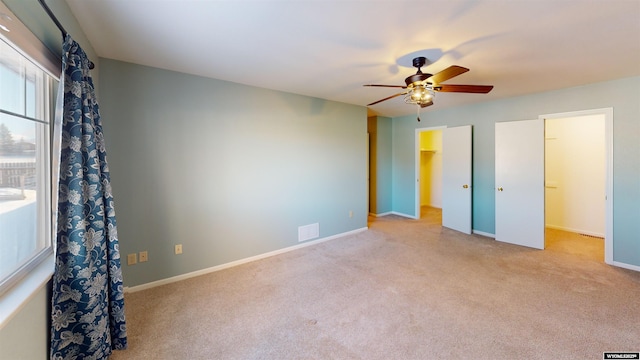 unfurnished bedroom featuring ceiling fan, light colored carpet, a spacious closet, and a closet