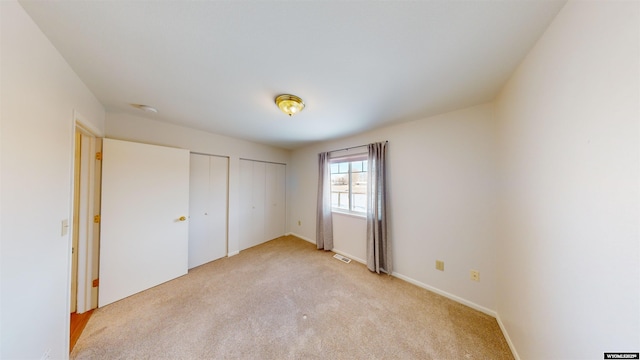 unfurnished bedroom with light colored carpet and two closets