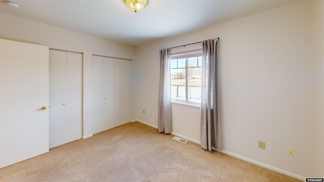 unfurnished bedroom with multiple closets and light carpet