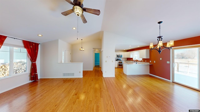 unfurnished living room featuring ceiling fan with notable chandelier, light hardwood / wood-style floors, sink, and vaulted ceiling