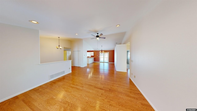 unfurnished living room featuring ceiling fan with notable chandelier, vaulted ceiling, and light hardwood / wood-style flooring