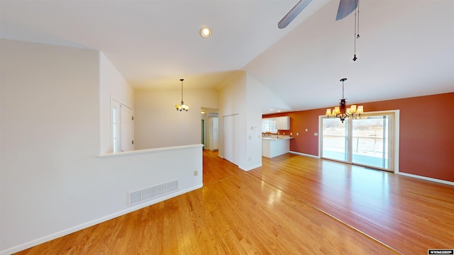 unfurnished living room featuring ceiling fan with notable chandelier, vaulted ceiling, and light wood-type flooring