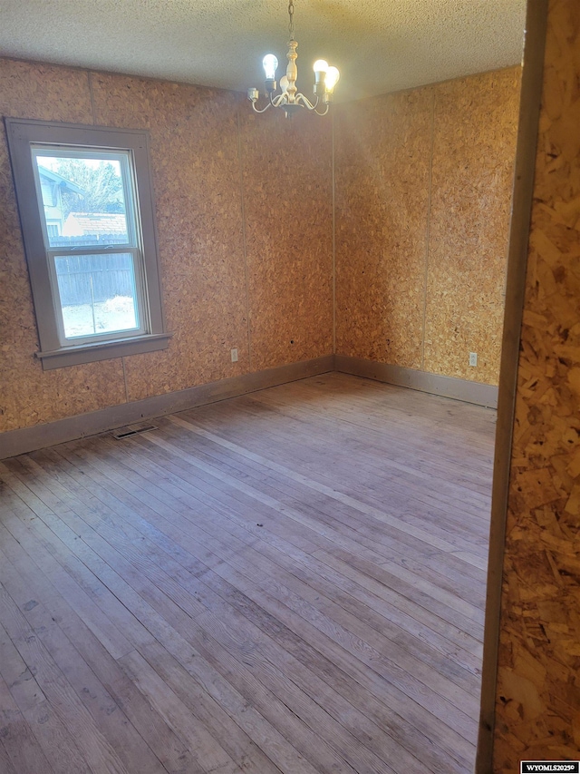 unfurnished room featuring a notable chandelier, a textured ceiling, and light hardwood / wood-style floors