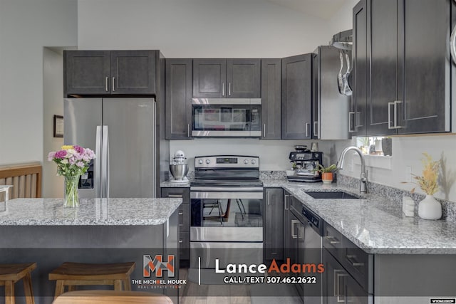 kitchen featuring a sink, vaulted ceiling, appliances with stainless steel finishes, light stone countertops, and a kitchen bar