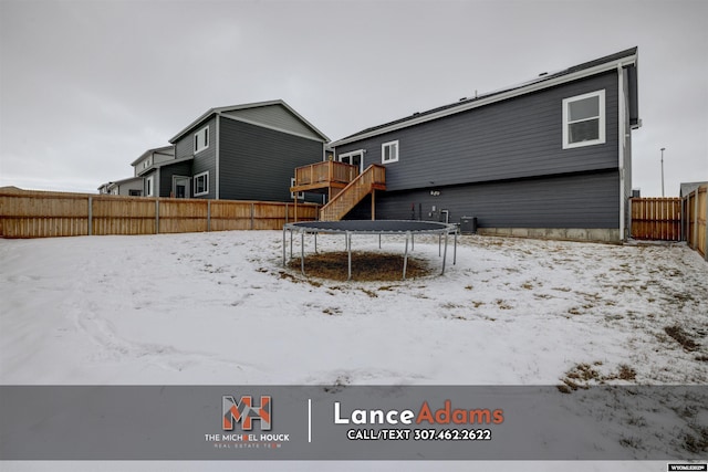 yard covered in snow with a deck and a trampoline