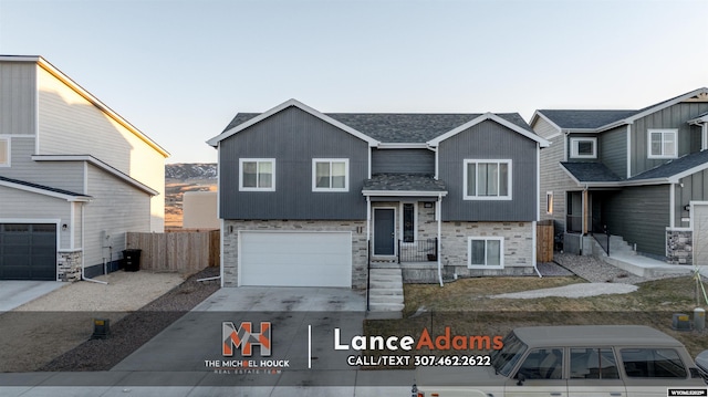 split foyer home featuring driveway, stone siding, an attached garage, and fence