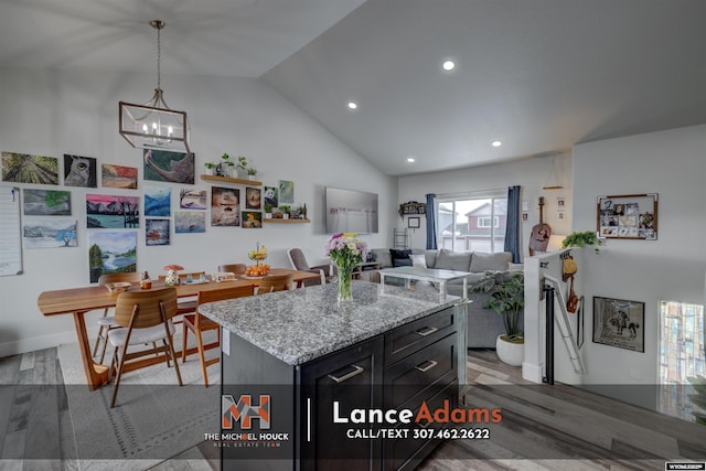 kitchen with light stone counters, a kitchen island, vaulted ceiling, and wood finished floors