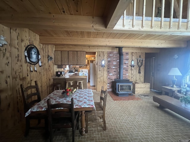 dining area featuring wood walls, beamed ceiling, a wood stove, and wood ceiling