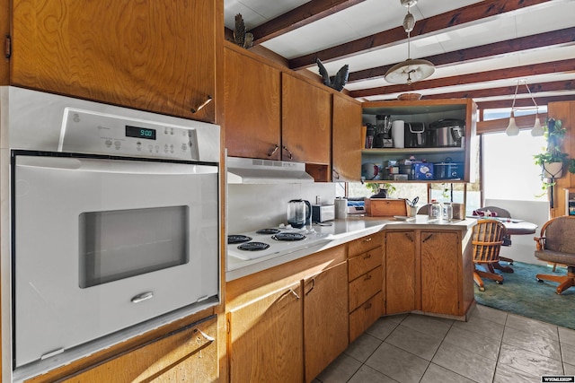 kitchen with light tile patterned flooring, white appliances, beam ceiling, and hanging light fixtures