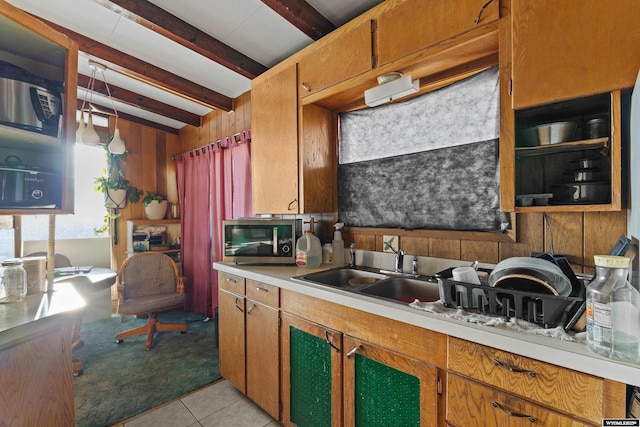 kitchen featuring sink, beam ceiling, light tile patterned flooring, and wood walls