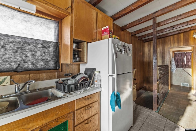 kitchen featuring sink, wooden walls, tile patterned floors, beamed ceiling, and white fridge