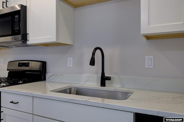 kitchen with gas range, light stone counters, white cabinetry, and sink