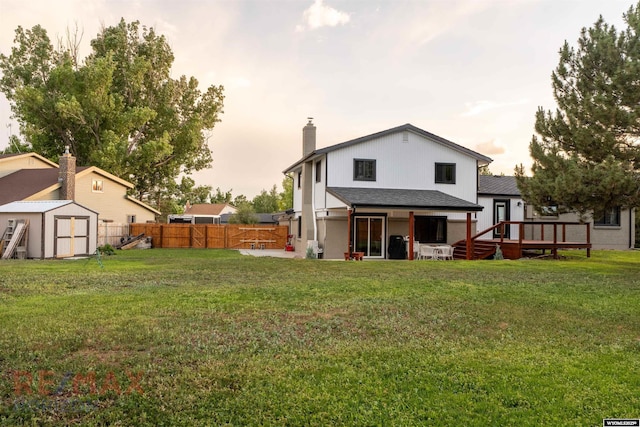 back house at dusk featuring a wooden deck, a yard, and a storage shed