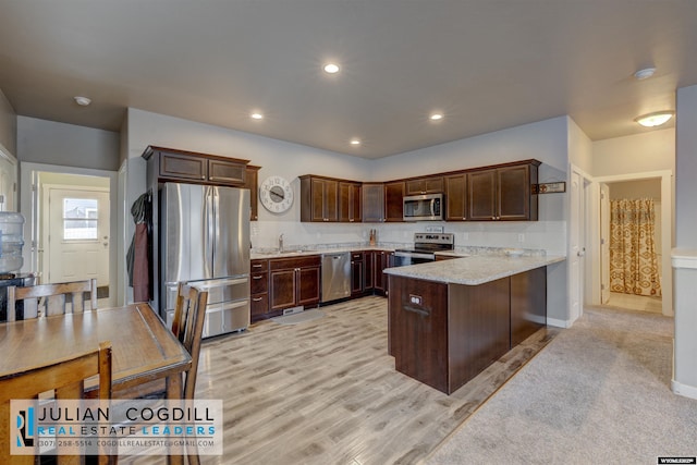 kitchen with dark brown cabinetry, light stone countertops, sink, stainless steel appliances, and kitchen peninsula