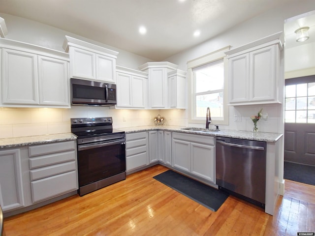 kitchen featuring white cabinetry, sink, light hardwood / wood-style floors, decorative backsplash, and appliances with stainless steel finishes