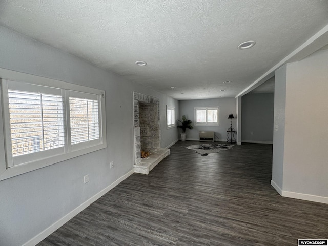 interior space with a textured ceiling, a stone fireplace, and dark wood-type flooring